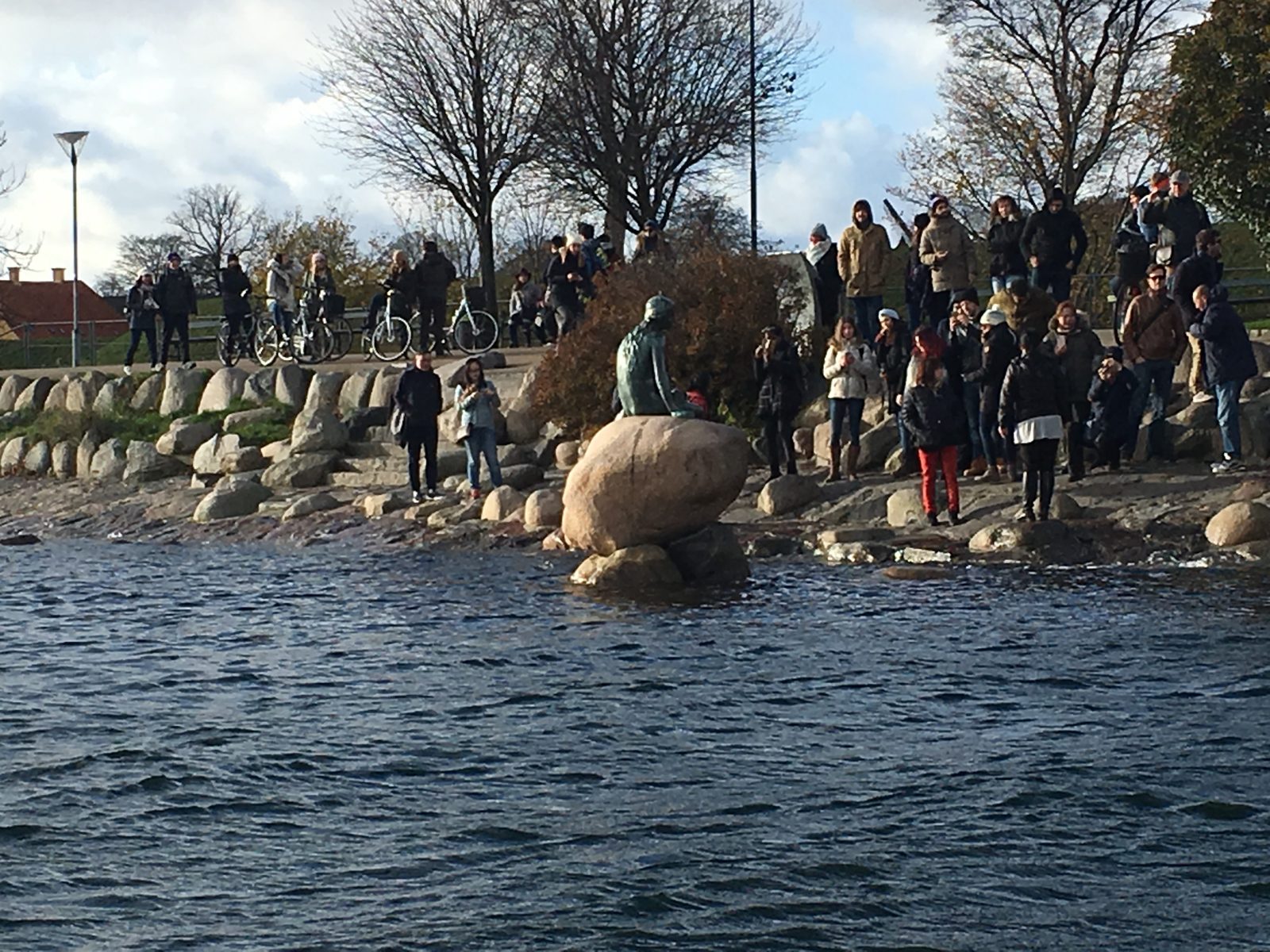 A crowd of visitors gathered on the rocks around the Little Mermaid bronze statue at the Copenhagen waterfront.