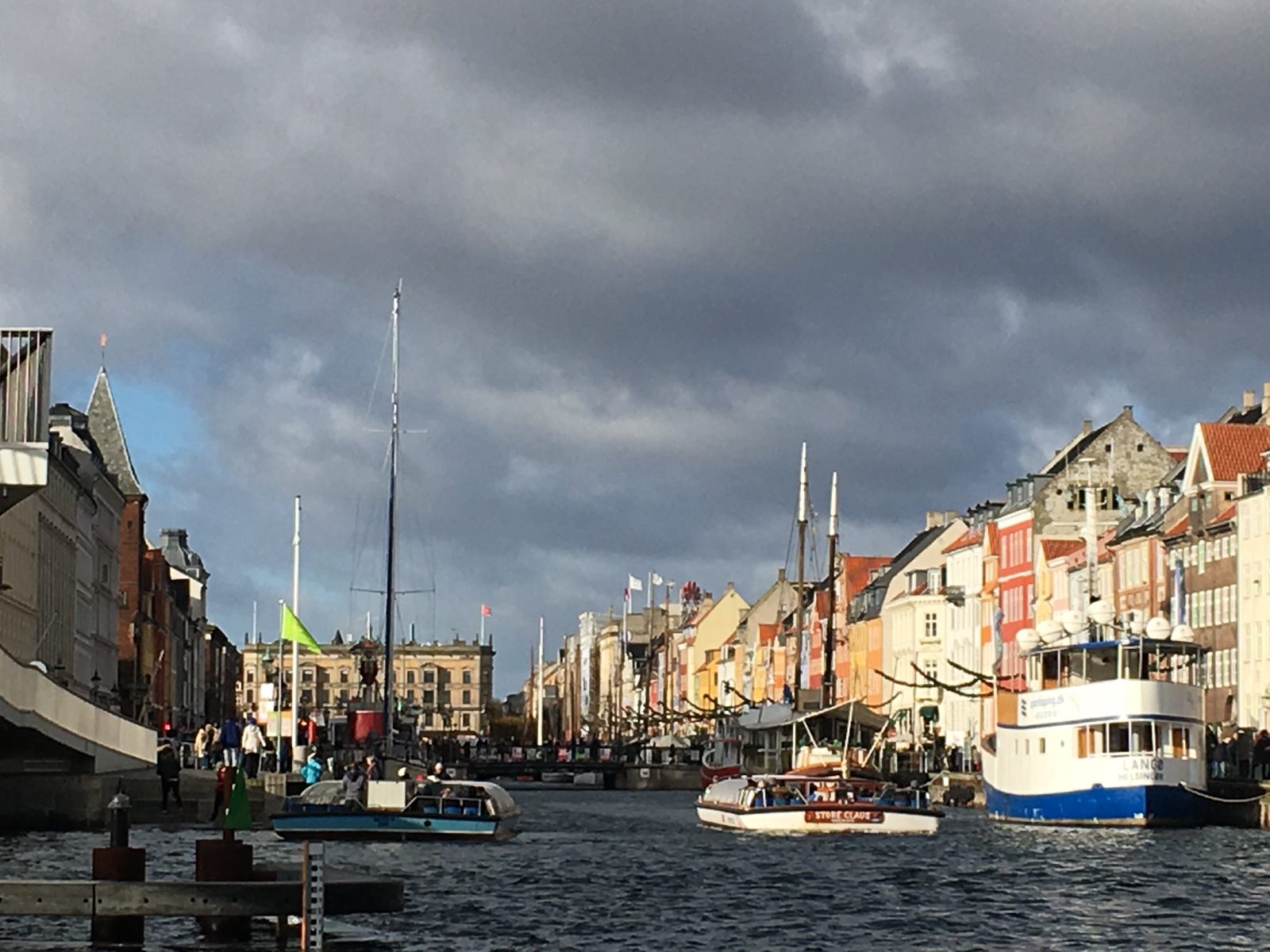 The colorful townhouses and moored boats at the mouth of the Nyhavn canal in Copenhagen under a dramatic cloudy sky.