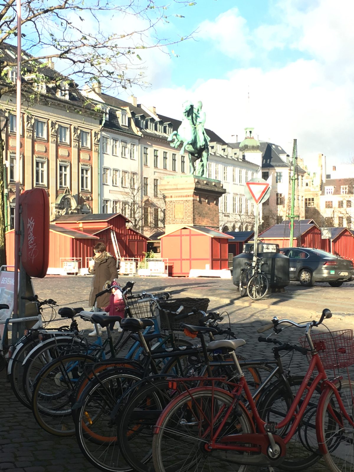 An equestrian bronze statue of Bishop Absalon on Højbro Plads, with red market huts, parked bicycles, and historic facades in warm sunlight.
